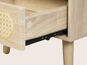 Primer plano de un mueble de madera clara con un elemento decorativo circular tejido en la parte frontal del cajón y patas cilíndricas de madera.