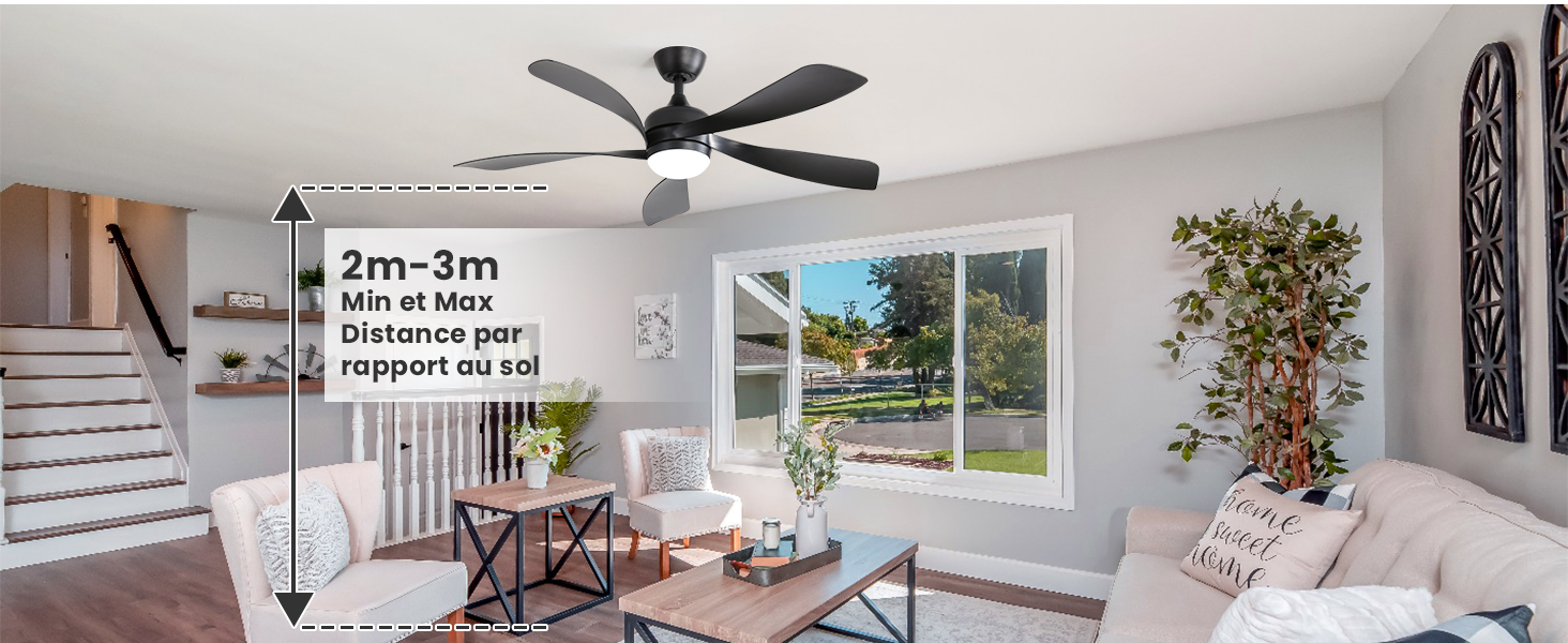 L'intérieur du salon moderne comprend un ventilateur de plafond à pales sombres monté sur un plafond blanc, des fenêtres lumineuses laissant entrer la lumière naturelle, des plantes vertes et un mobilier contemporain.