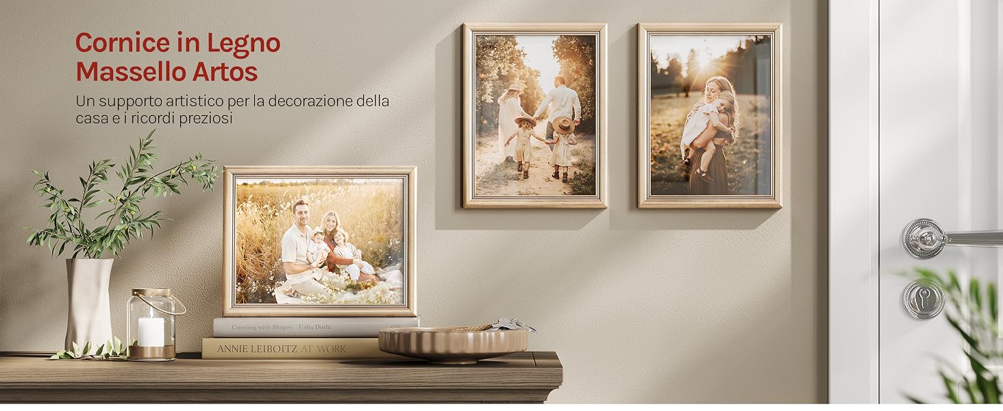 Il testo recita 'Cornice in Legno Massello Artos'. Tre opere d'arte incorniciate esposte sopra una mensola in legno con fiori bianchi in vaso e accessori per l'arredamento.