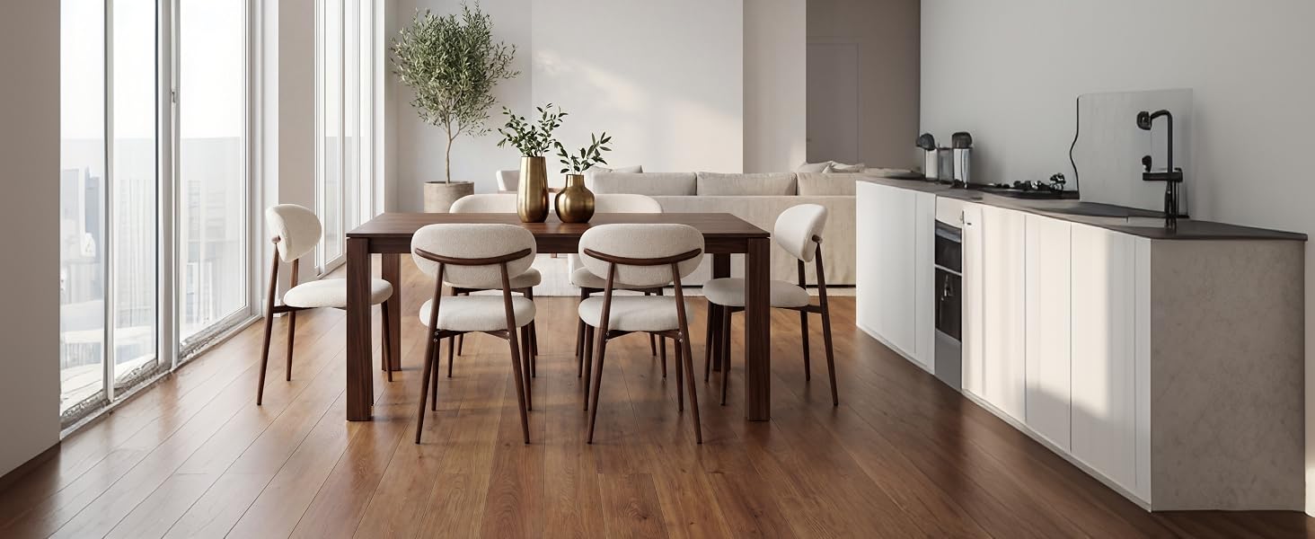 Cuisine-salle à manger moderne avec table en bois foncé, chaises beiges, armoires blanches, évier en acier inoxydable et fenêtres lumineuses.