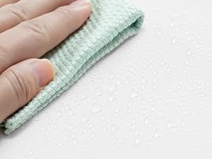 Primo piano di una mano che tiene un panno in microfibra verde chiaro su uno sfondo bianco, a dimostrazione