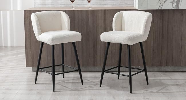 Zwei moderne Barhocker mit cremefarbener, gepolsterter, geschwungener Rückenlehne, gepolsterten Sitzen und schwarzen Metallbeinen an der Kücheninsel.