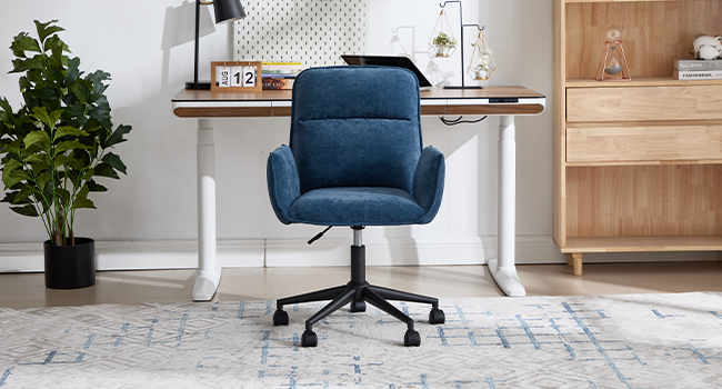 Modern home office setting with blue upholstered office chair, wooden desk, and decorative potted plant against light walls with minimalist decor.