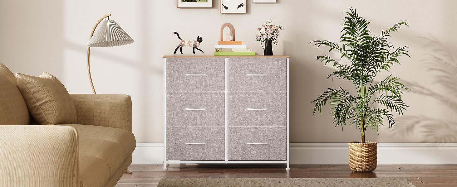 Commode grise moderne avec des objets décoratifs sur le dessus, positionnée contre un mur blanc avec une plante en pot à côté.