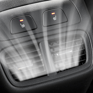 Car interior detail showing two heated seat buttons and air vents. Buttons have orange indicator lights and seat icons. Textured dashboard visible.