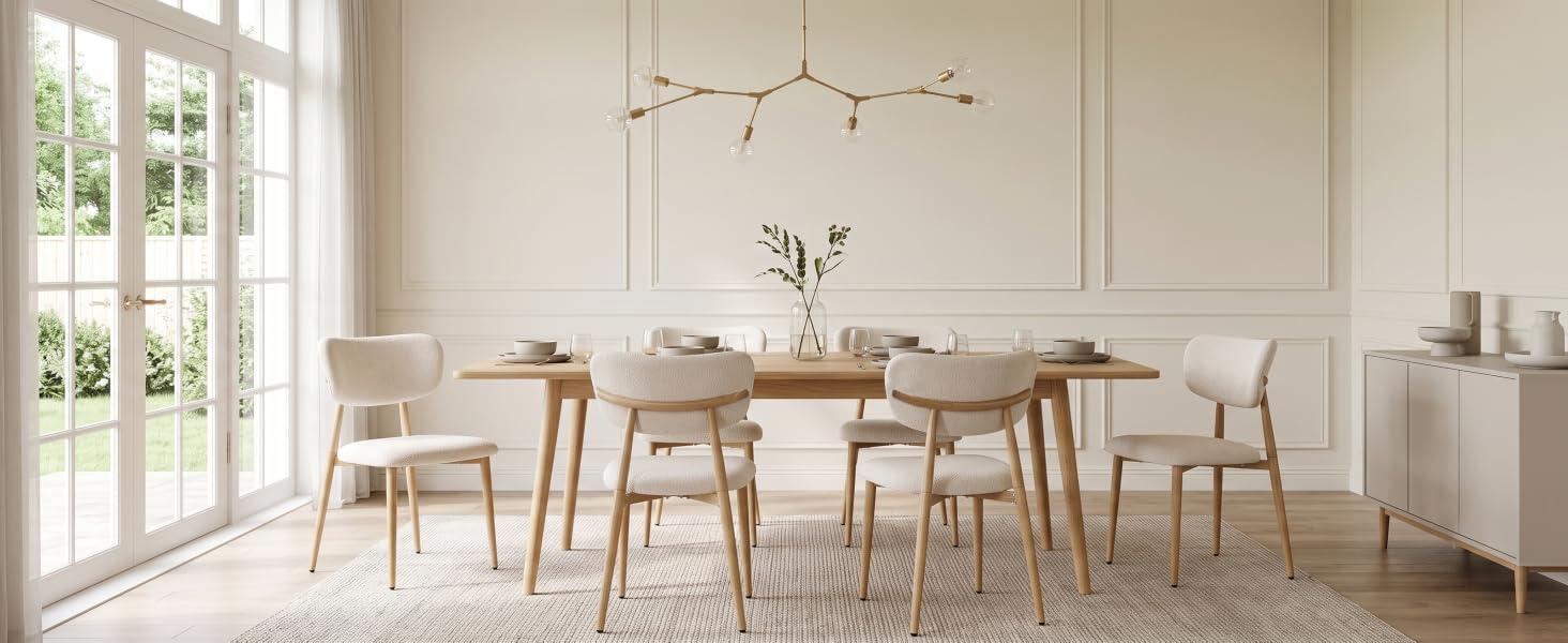 Salle à manger lumineuse et minimaliste avec table et chaises en bois, lampes suspendues, murs blancs et lumière naturelle provenant de grandes fenêtres et portes vitrées.