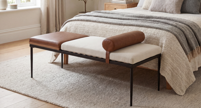 Modern bedroom furniture piece: mid-century style wooden bench with cream/beige upholstered cushioned seat, dark wood legs and frame, positioned at foot of bed with gray bedding and beige headboard.