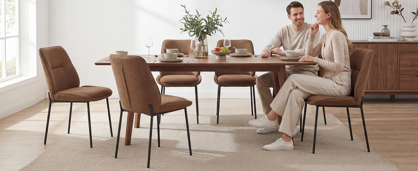 Sala da pranzo moderna con tavolo rotondo in legno, quattro sedie imbottite marroni e credenza in legno abbinata. Due persone sedute al tavolo in un set di mobili contemporanei dai toni neutri.