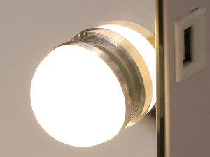 Close-up of a round, illuminated light fixture mounted on a wall. The fixture has a metallic rim and emits a warm, white glow.