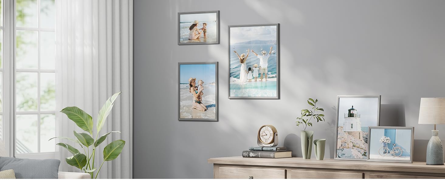 Decorazione murale interna con più fotografie incorniciate disposte su una parete grigia sopra mobili in legno con oggetti decorativi e vegetazione.