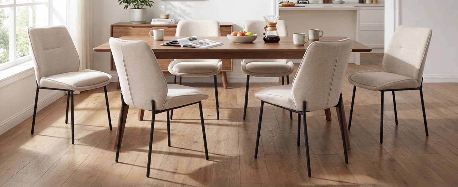 Set da pranzo composto da tavolo rotondo in legno con sei sedie imbottite in tessuto beige/crema con gambe in metallo, esposte in un luminoso interno della cucina.
