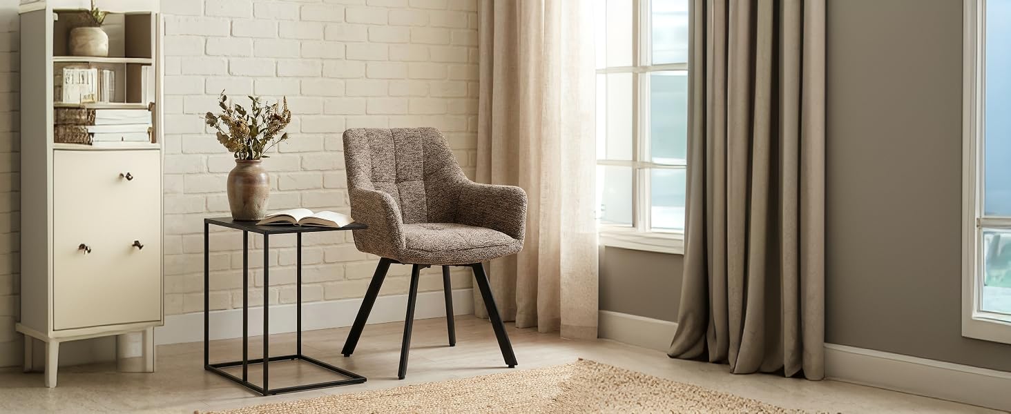 Aménagement intérieur de la pièce comprenant un fauteuil rembourré gris, une table d'appoint ornée de fleurs et des rideaux allant du sol au plafond dans une chambre ou un espace de vie minimaliste.