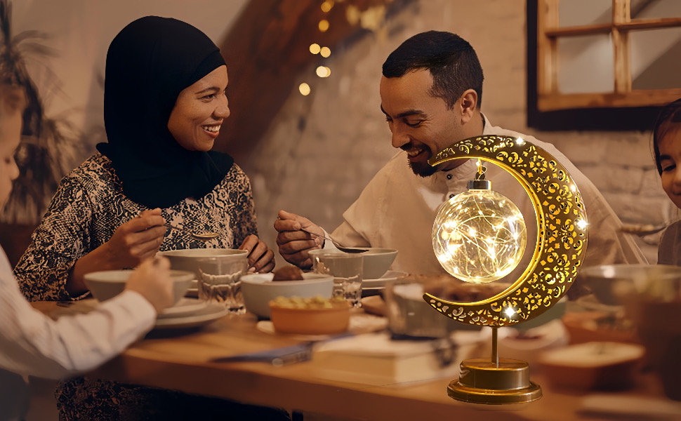 Due persone sedute a un tavolo con una lampada decorativa a forma di mezzaluna dorata che fornisce un'illuminazione ambientale.