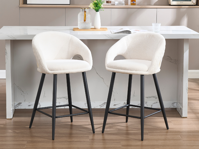 Comedor moderno con sillas tapizadas en blanco con patas de metal negro, dispuestas alrededor de un mostrador o mesa blanca en un ambiente interior minimalista.