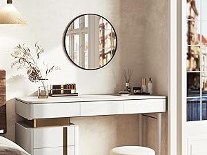 Moderno tocador blanco con tres cajones, detalles dorados y laterales con espejos. Espejo circular en la parte superior, taburete de color crema y elementos decorativos sobre la mesa en
