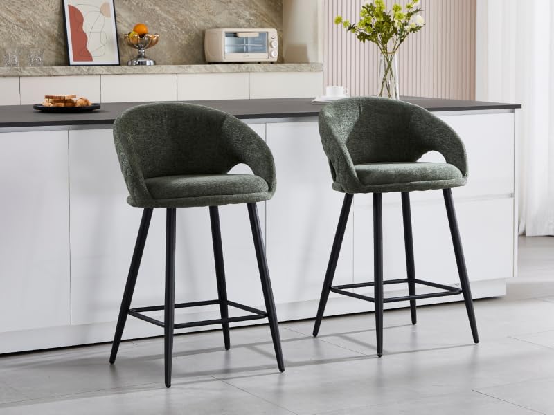 Due moderni sgabelli da bar rivestiti in velluto di colore verde scuro con schienali curvi a botte e gambe in metallo nero, posizionati su un bancone da cucina bianco con piano di lavoro scuro.