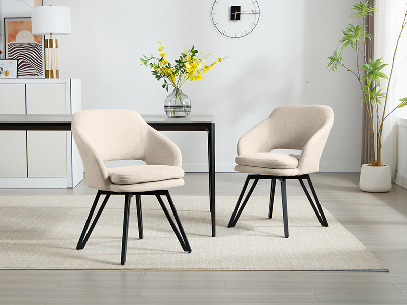 Zwei beige gepolsterte Esszimmerstühle mit geschwungenen Rückenlehnen und Sitzen. Schwarze Metallbeine mit abgewinkeltem Design. Stühle neben einem schwarzen Tisch in einem modernen Wohnraum