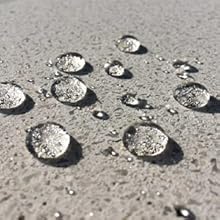 Photographie rapprochée de gouttelettes d'eau sur une surface de béton gris, démontrant des propriétés hydrofuges ou hydrophobes