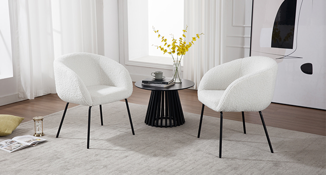 Deux fauteuils incurvés blancs avec revêtement texturé flou et pieds en métal noir, flanquant une petite table d'appoint ronde noire avec sommier à lattes dans un décor intérieur lumineux