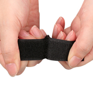 Hands demonstrating a small, black, elastic finger support or brace being stretched between thumb and forefinger.