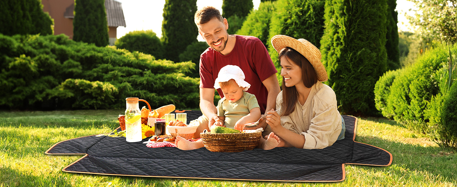 Outdoor picnic scene in a garden with people sitting on blanket surrounded by lush greenery and hedges.