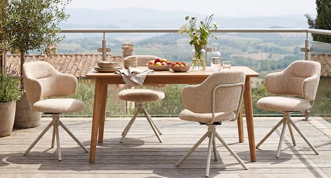 Salle à manger extérieure sur une terrasse avec table en bois, quatre chaises rembourrées beiges avec bases pivotantes, couverts et vue panoramique sur le paysage en arrière-plan.