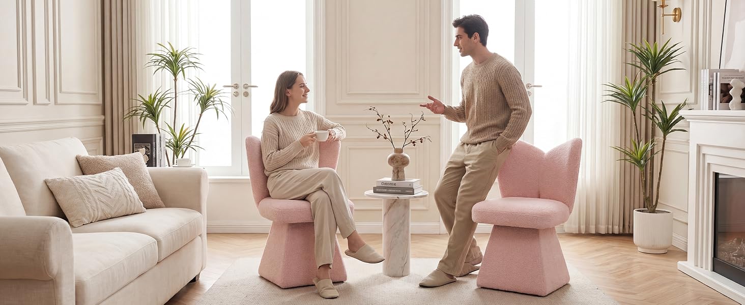 Two adults and child in bright living room with pink ottoman seating, potted plants, natural light from windows, casual family setting.