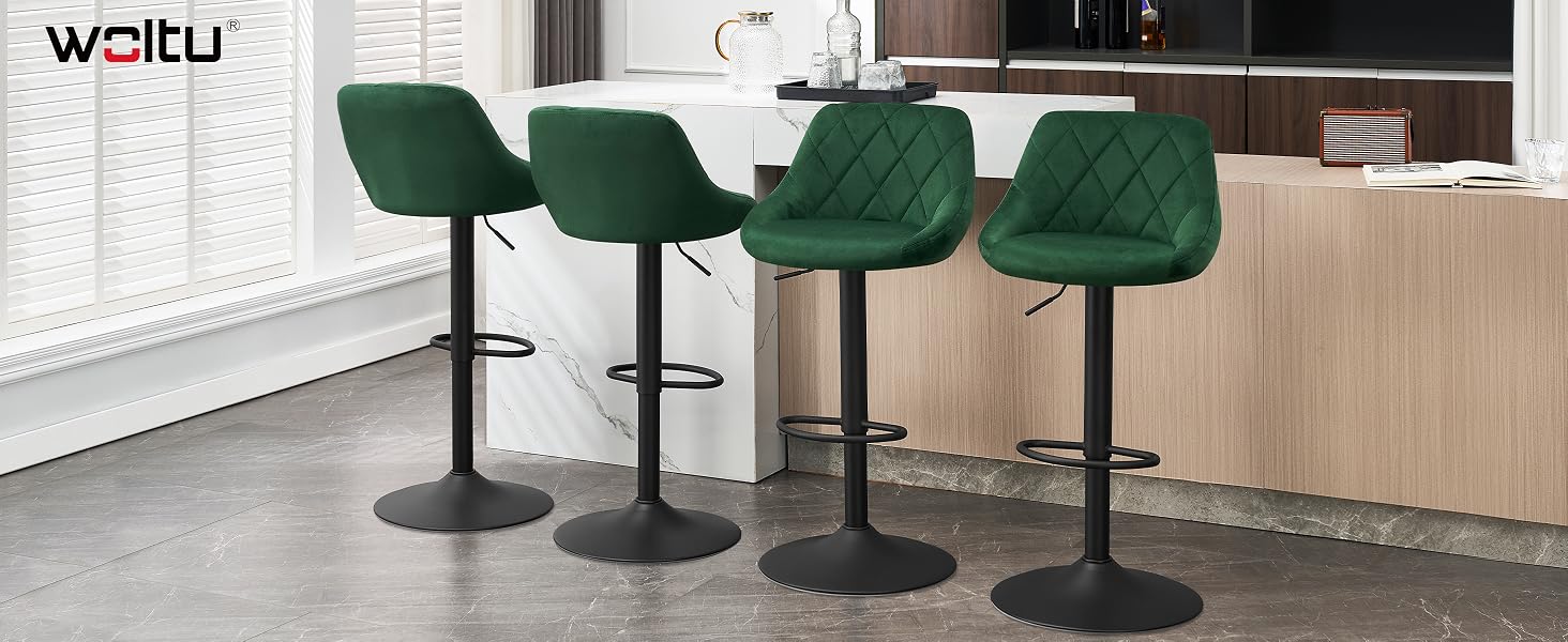 Four green velvet bar stools with quilted backrests and black metal bases, arranged in a row at a wooden kitchen counter.