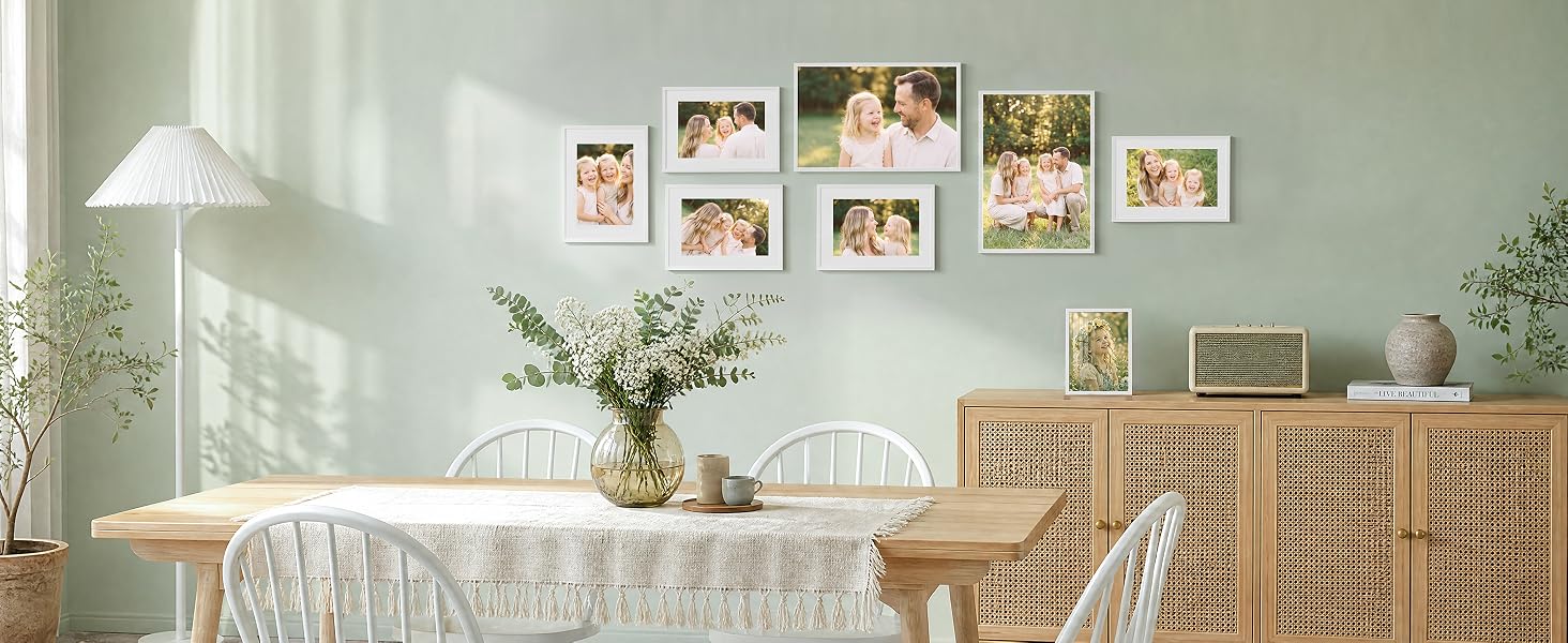 Innenraum mit hellgrüner Wand, auf der eine Galerie mit gerahmten Fotografien ausgestellt ist. Naturholzmöbel, weiße Bettwäsche, frische Blumen in der Vase und geflochtene Aufbewahrungskörbe sorgen für eine minimalistische Inneneinrichtung.