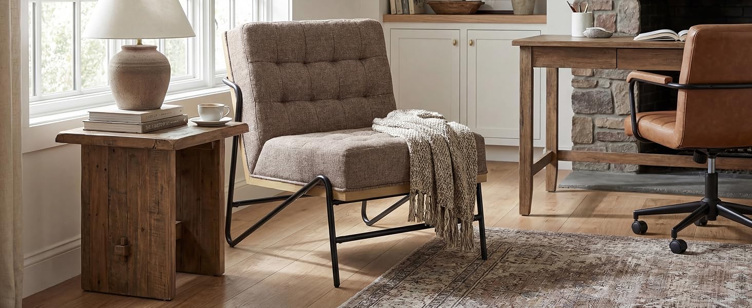 Scena domestica interna con disposizione dei mobili con sedia imbottita, tavolo rotondo in legno e illuminazione a sospensione. Espositore decorativo per soggiorno dai toni neutri che mostra mobili e prodotti per l'illuminazione.