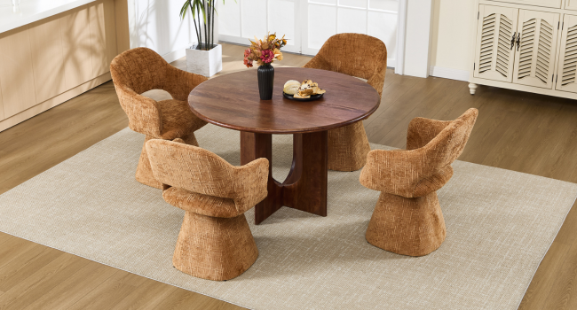 Ambiente interno con tavolo da pranzo rotondo in legno circondato da quattro sedie in rattan intrecciato su pavimento in legno con illuminazione naturale.