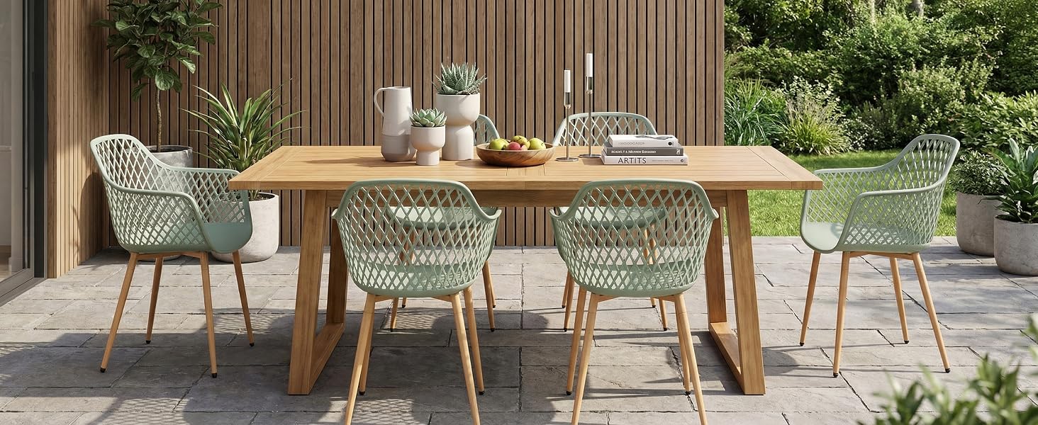 Terrasse extérieure avec table à manger en bois et quatre chaises tissées vert menthe sur un pavage en pierre, soutenues par une clôture en bois.