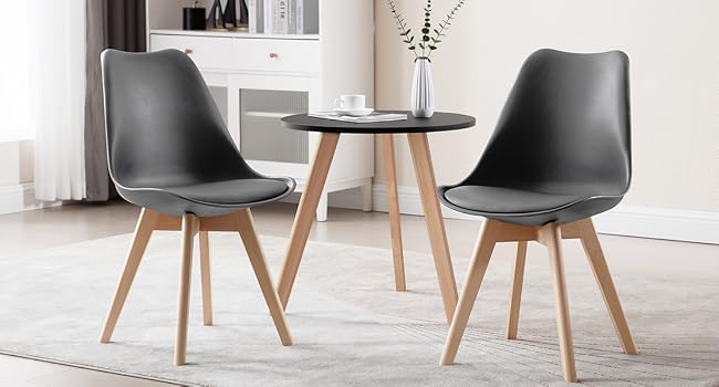 Modern dining set with round black table and two gray chairs. Chairs have molded seats, cushions, and wooden legs. Table has wooden tripod base.