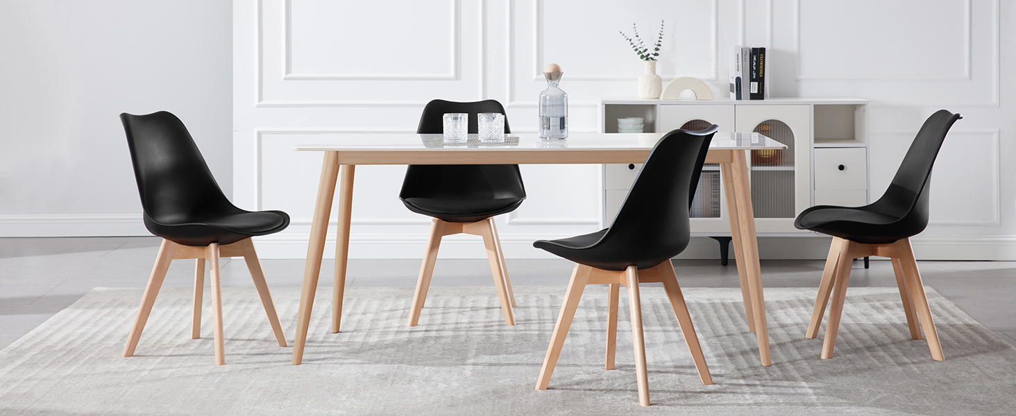 Juego de comedor moderno con mesa de madera y cuatro sillas negras con asientos moldeados y patas de madera en una habitación blanca.