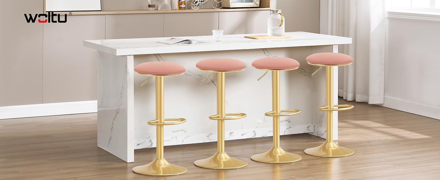 Isola da cucina bianca con quattro sgabelli da bar in velluto rosa con basi dorate. Gli sgabelli hanno sedili rotondi e sono posizionati davanti a un piano di lavoro elegante