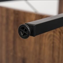Primer plano de una pata de mueble ajustable negra con una tapa circular, colocada sobre una superficie de madera
