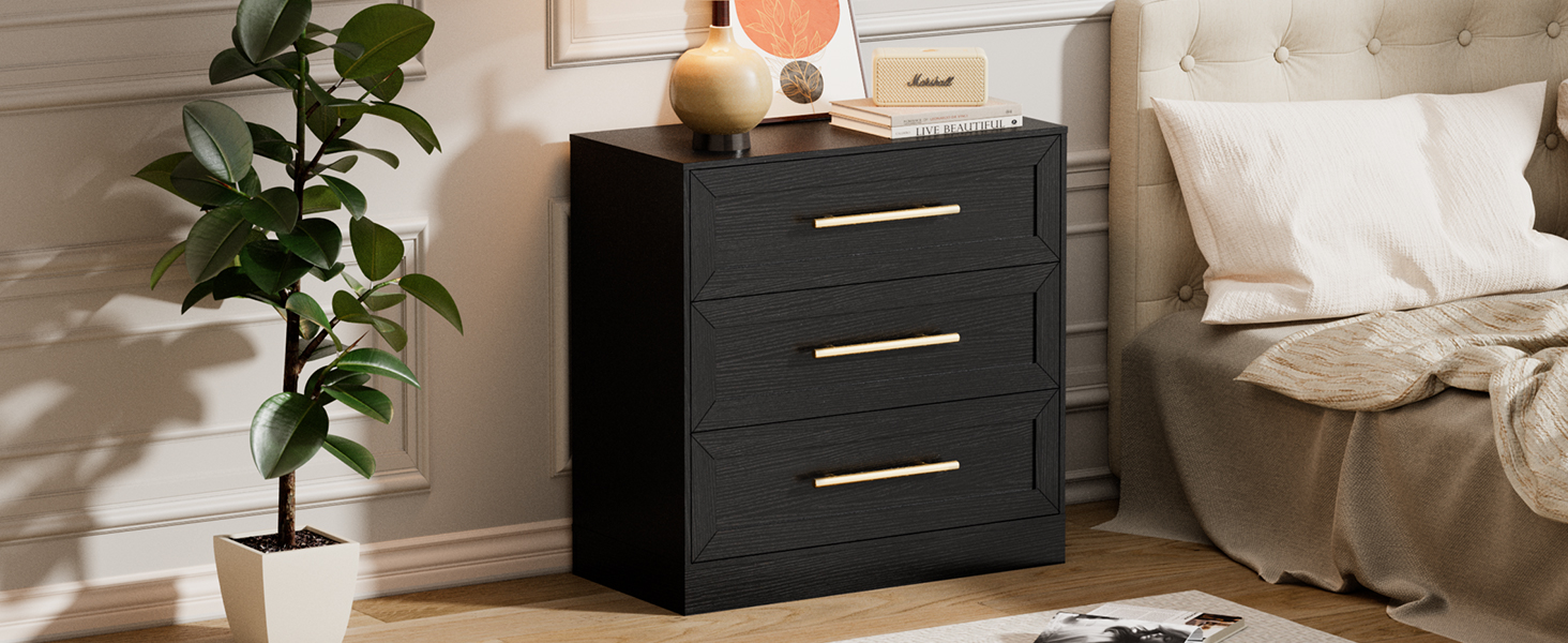 Comodino o comò moderno nero con maniglie argentate mostrato nella camera da letto, con decorazioni a forma di piante d'appartamento e biancheria da letto bianca sullo sfondo.
