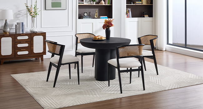 Moderno juego de comedor con mesa redonda negra con sillas de madera que combinan marcos negros y respaldos de caña tejidos, dispuestos sobre una alfombra con motivos geométricos claros.