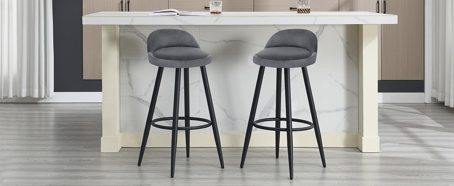 Dos taburetes de bar tapizados en gris con respaldos curvos y patas de metal negro, colocados en una encimera o isla blanca en una cocina moderna