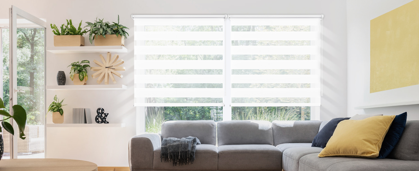 Salon moderne avec canapé gris, coussins décoratifs jaunes et stores blancs. Des étagères en bois présentent des plantes et des objets de décoration.