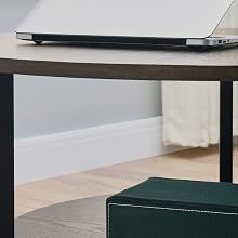 Round coffee table with wood top and black metal frame. Two-tier design with laptop on upper surface and green ottoman underneath.