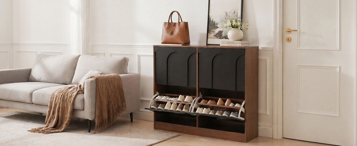 Salon moderne avec canapé rembourré gris clair, couverture marron, armoire de rangement noire avec étagères ouvertes présentant des objets de décoration et des livres, murs de couleur crème et parquet.