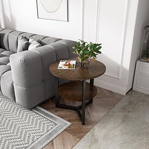 Wohnzimmerecke mit einem grauen Ecksofa, einem runden Beistelltisch aus Holz mit zwei Ebenen und einer Topfpflanze. Teppich mit Chevronmuster, sichtbar auf