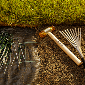 Outils de jardinage sur terre : râteau en métal à long manche, matériau en tissu ou en maille et pointes ou clous en métal. De l'herbe verte est visible en haut.