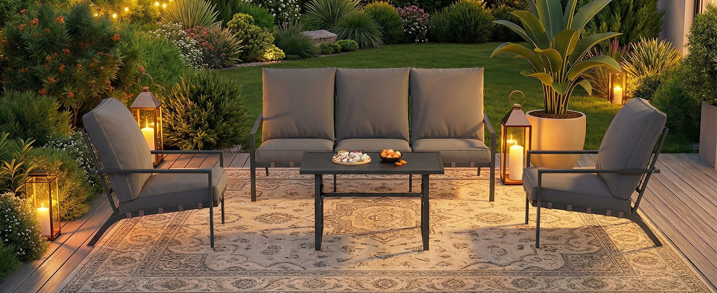 Outdoor patio furniture set featuring dark gray cushioned seating arranged around coffee table. Evening/dusk setting with ambient lighting in garden environment.