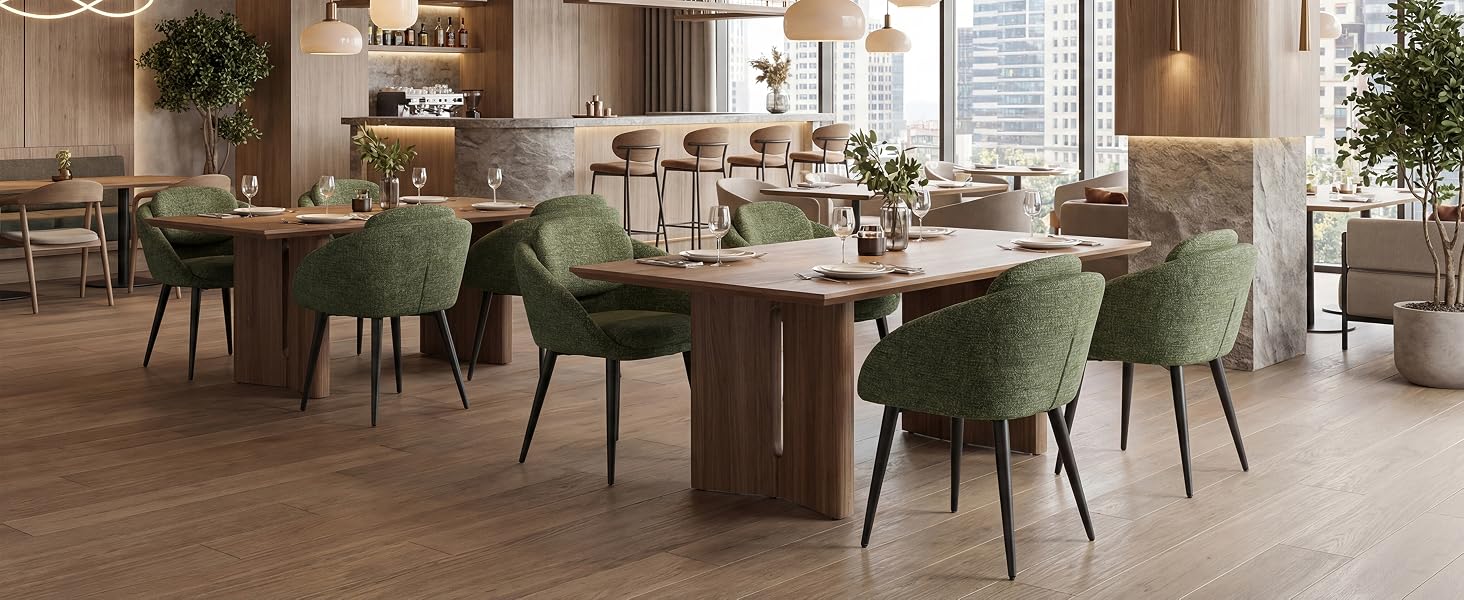 Interno moderno del ristorante con pavimento in legno, con morbide sedie da pranzo in velluto verde disposte attorno a tavoli circolari in un ambiente spazioso e ben illuminato.