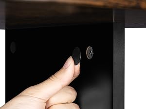 Primer plano de una mano que presiona un pequeño botón circular negro sobre una superficie oscura, probablemente parte de un mueble o dispositivo electrónico