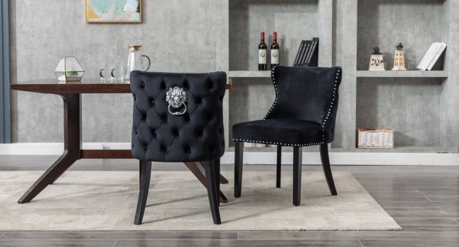 Due sedie da pranzo in velluto nero con schienale trapuntato, borchie argentate e battenti decorativi a testa di leone. Posizionato vicino a un tavolo di legno in una moderna sala da pranzo