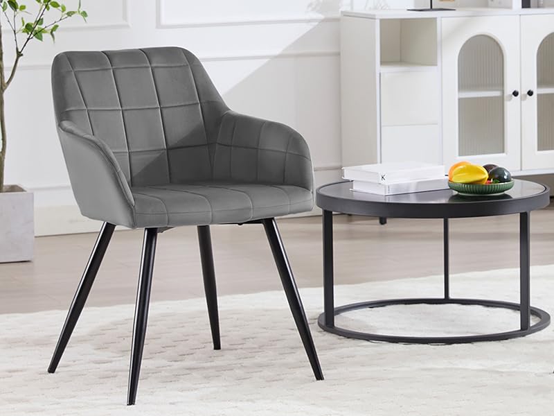 de terciopelo gris con respaldo acolchado y patas de metal negro, junto a una mesa de centro redonda negra en un moderno salón