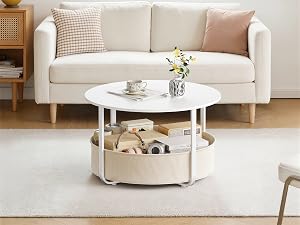 Sofá tapizado de color crema con reposabrazos acolchados colocado en una luminosa sala de estar con una mesa de centro redonda blanca en la parte inferior, una cesta de almacenamiento tejida en la parte inferior, una ventana con luz natural detrás, un estilo minimalista de decoración del hogar.